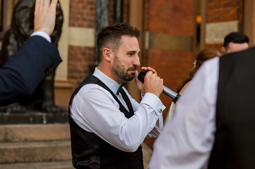 Person in formal attire singing into microphone on brick building steps.
