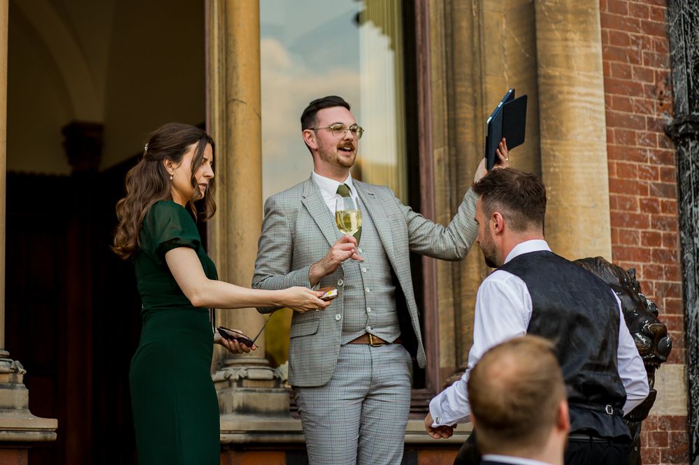 Wedding guests mingle and celebrate on an elegant brick building patio with stone columns.