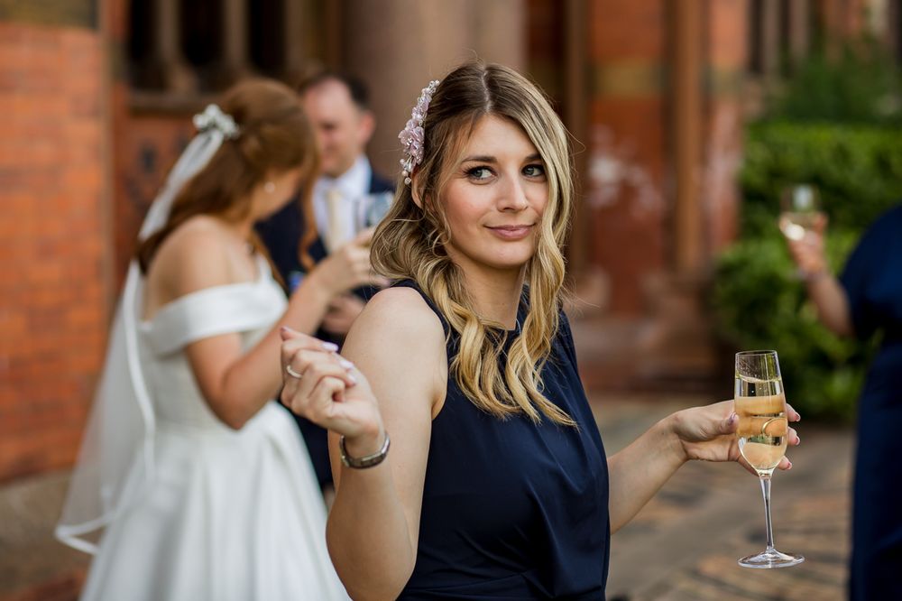 Guest in navy dress enjoying champagne at outdoor wedding reception.