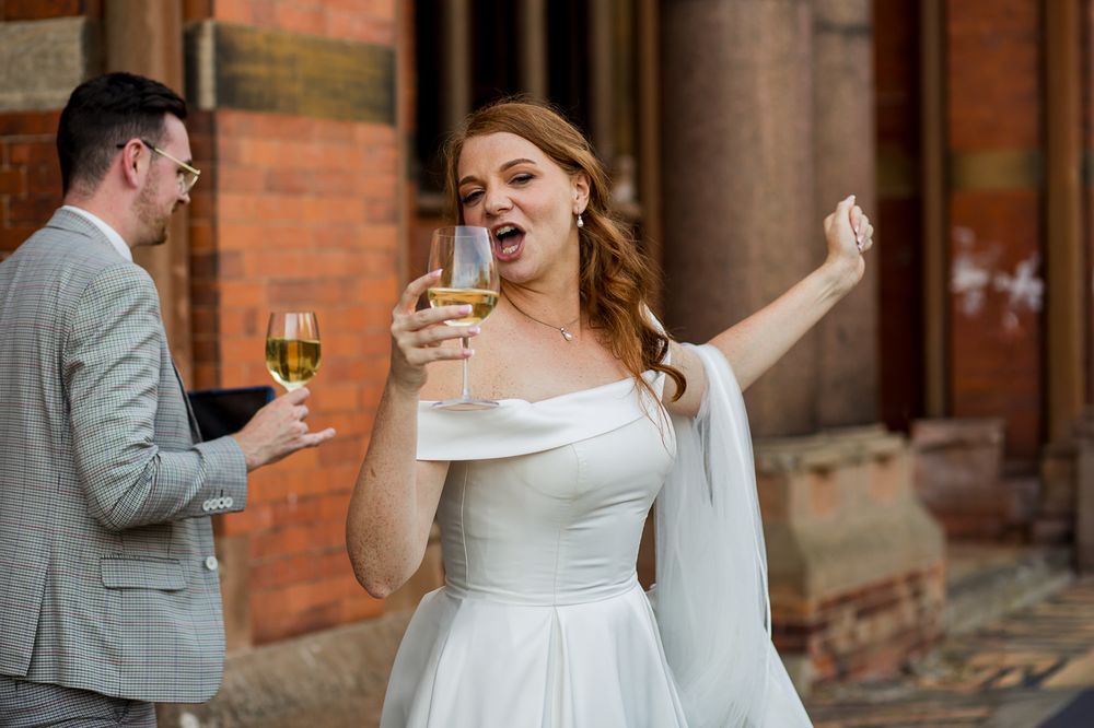 Wedding celebration with guests enjoying drinks outside a classic brick building.
