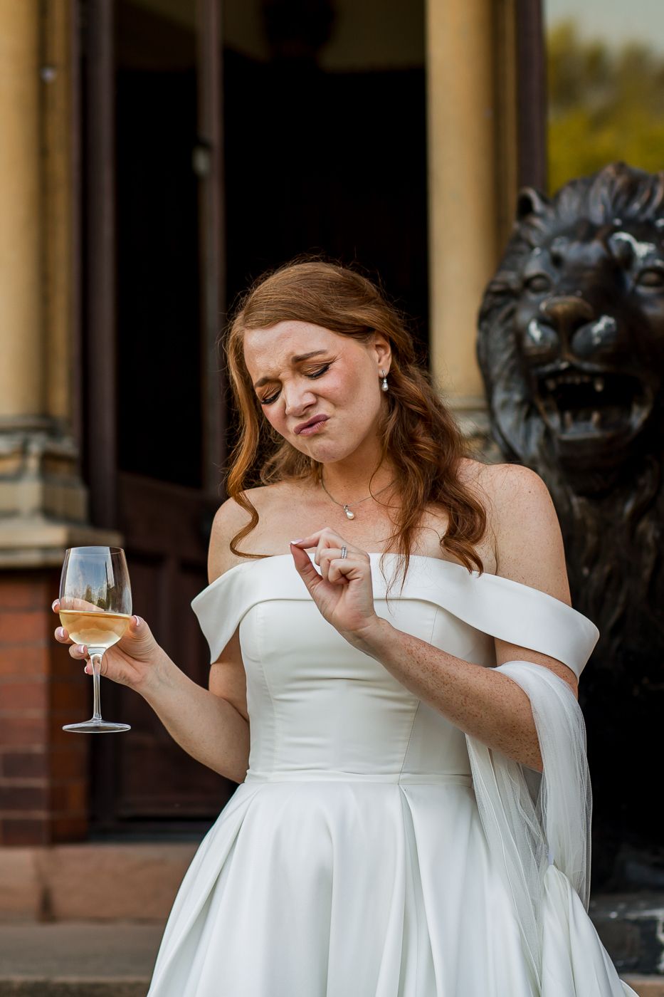 Woman in white wedding dress poses dramatically with wine glass on stone steps.