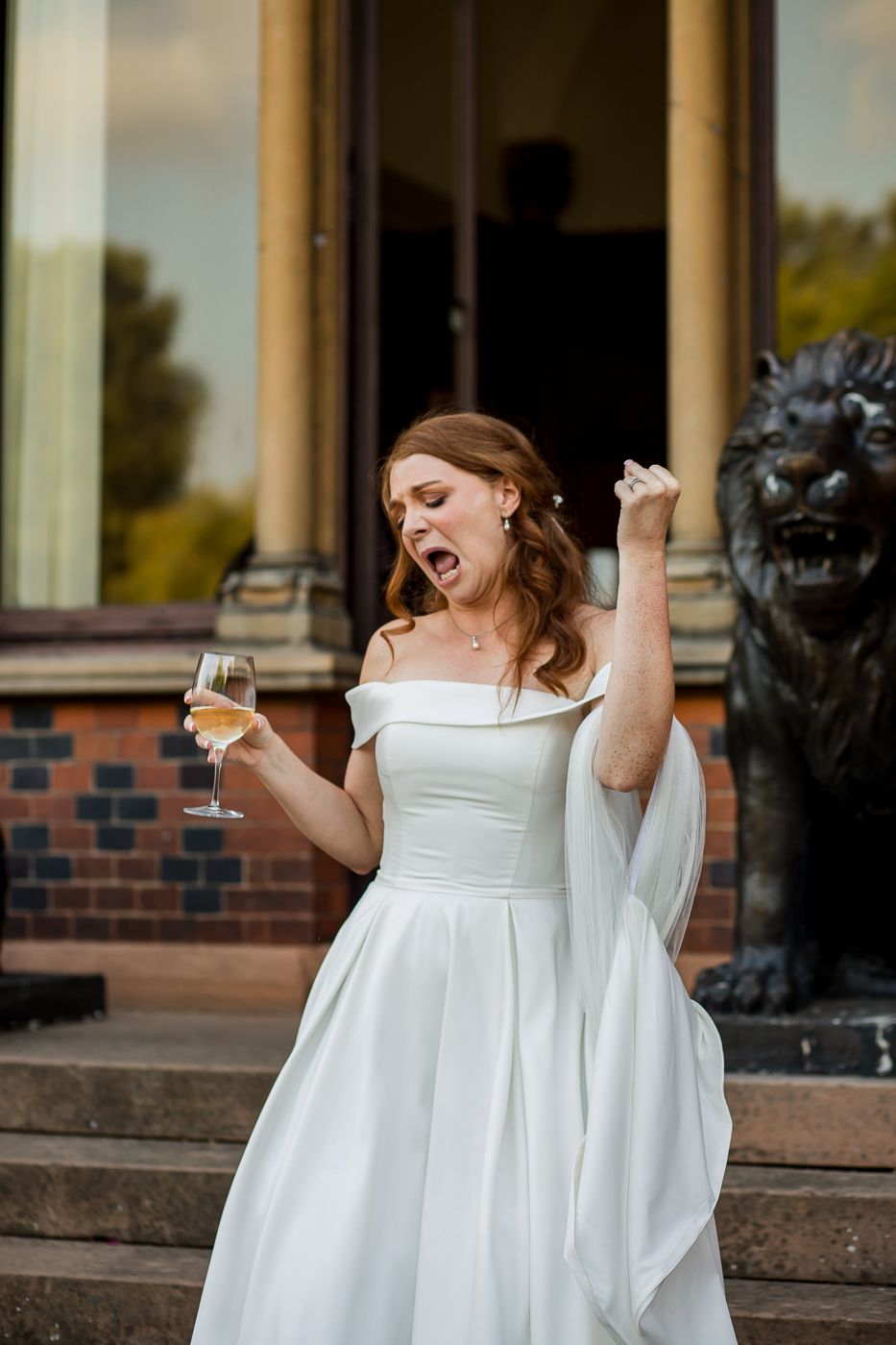 Bride in flowing white dress dances joyfully on stone steps of brick building.