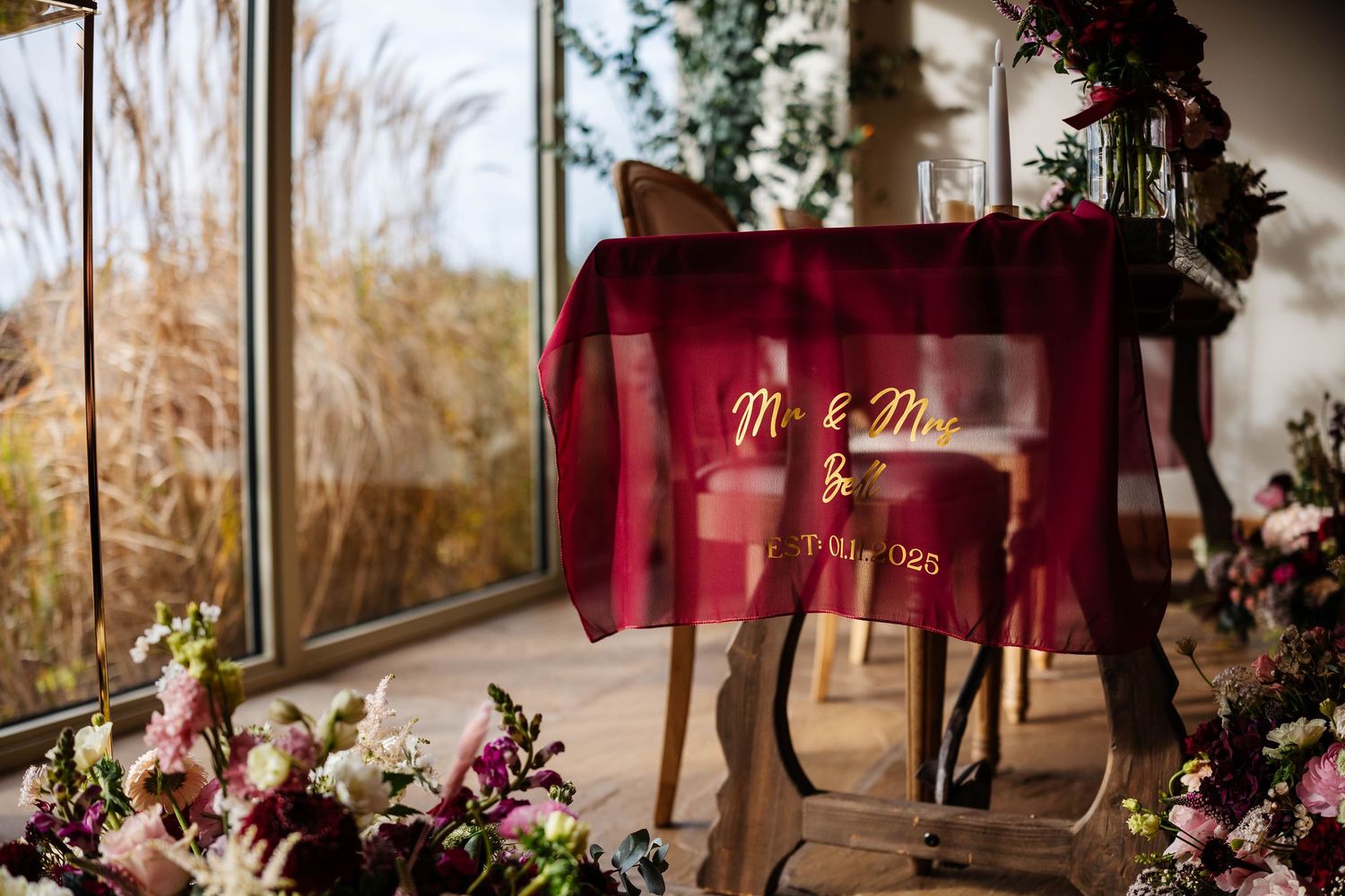 Wedding reception decor features burgundy and purple floral arrangements with elegant table settings in a rustic venue at Hobbit Hill