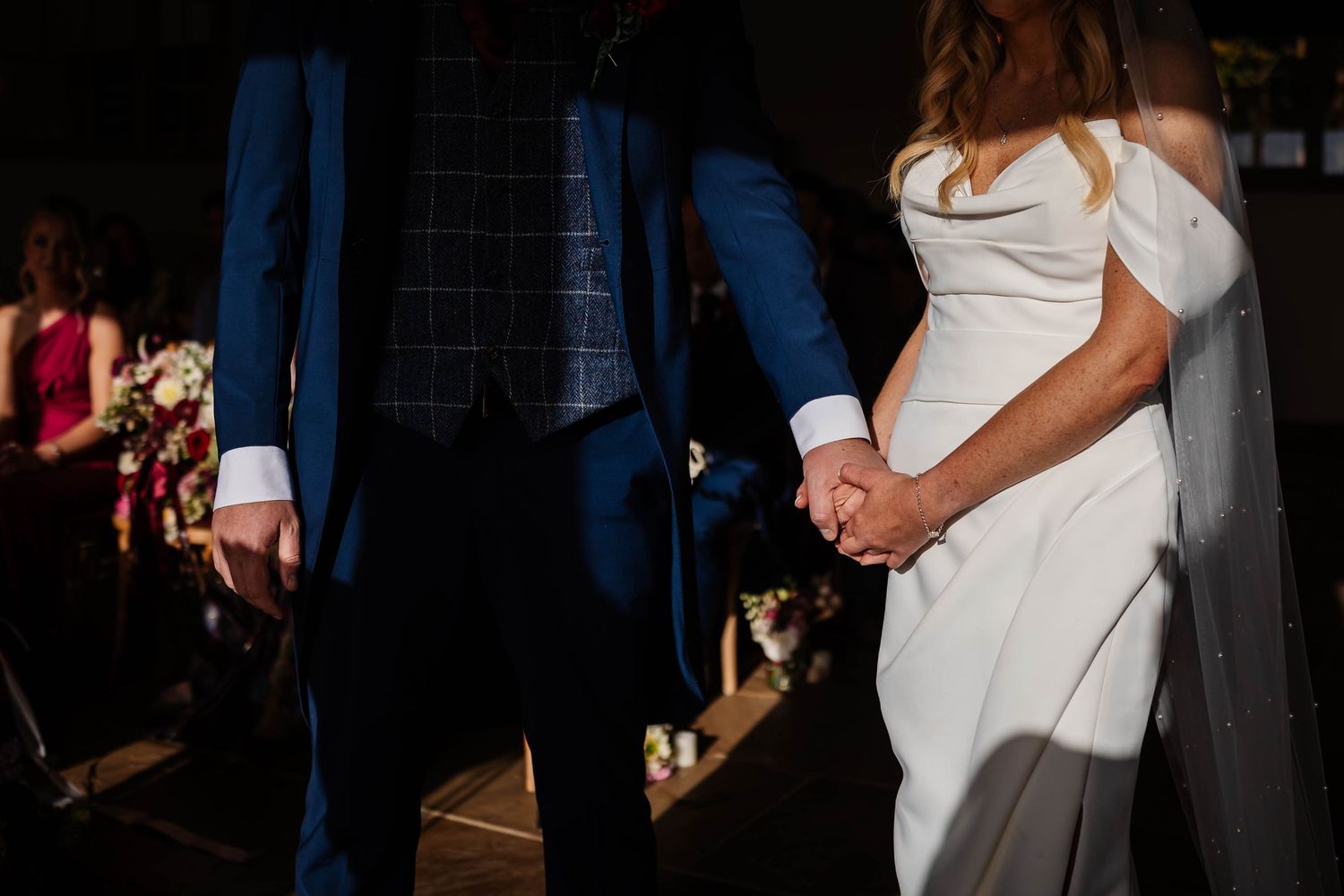 Close-up view of a couple in wedding attire standing together in dramatic lighting at an indoor venue at Hobbit Hill by Lynette Matthews