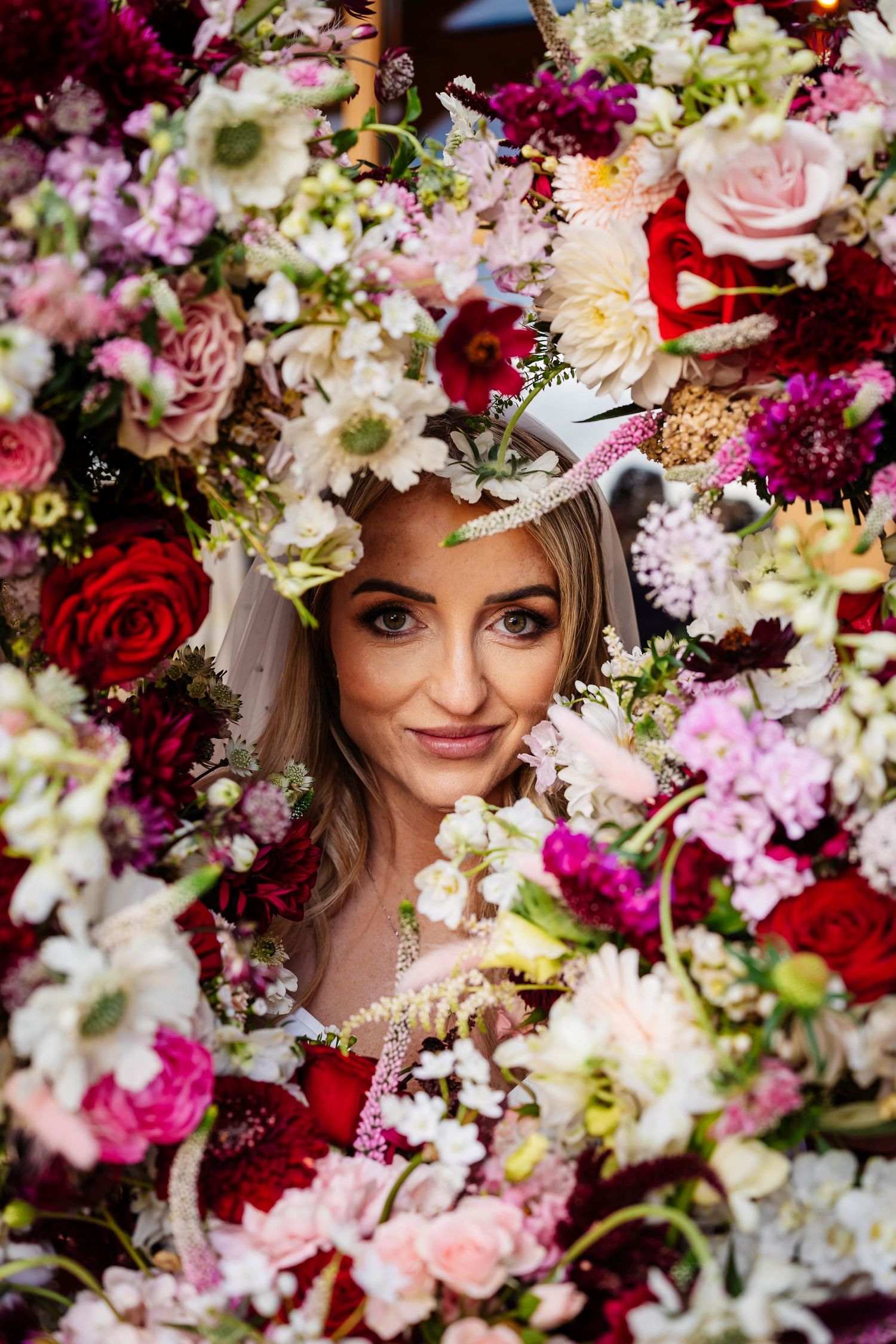 A romantic floral arrangement features pink, white, and deep red blooms with lush greenery in an elegant wedding display.