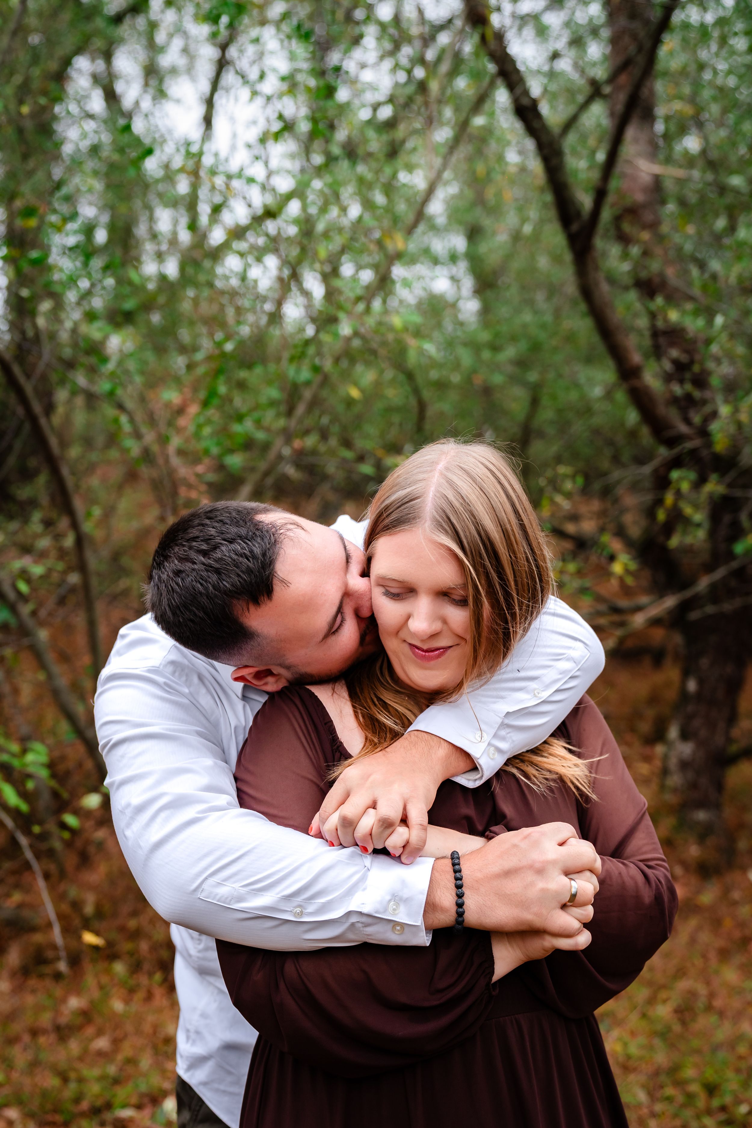 Playful engagement photos in a wooded area with natural lighting.