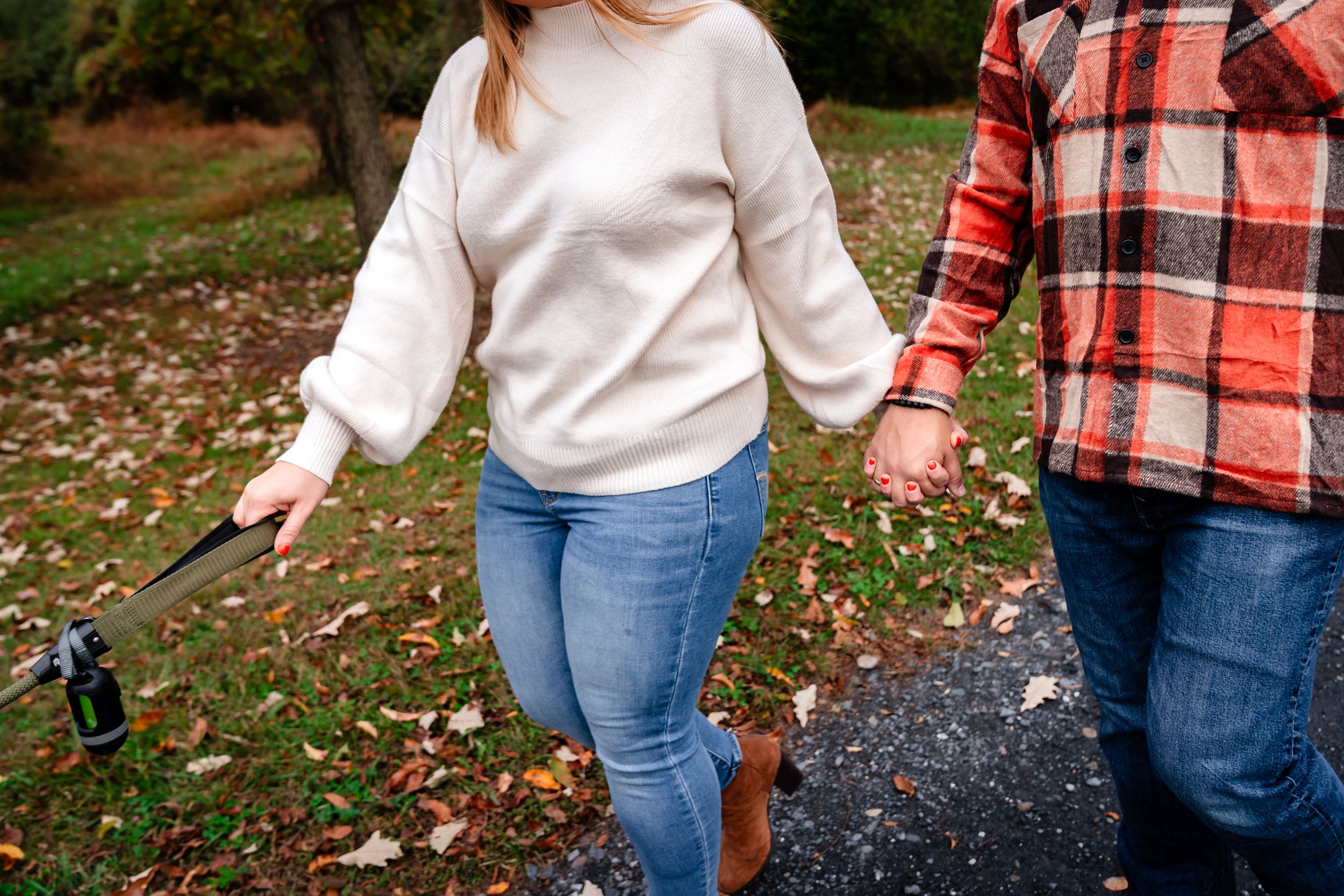 Close-up of couple holding hands while walking through fallen autumn leaves.