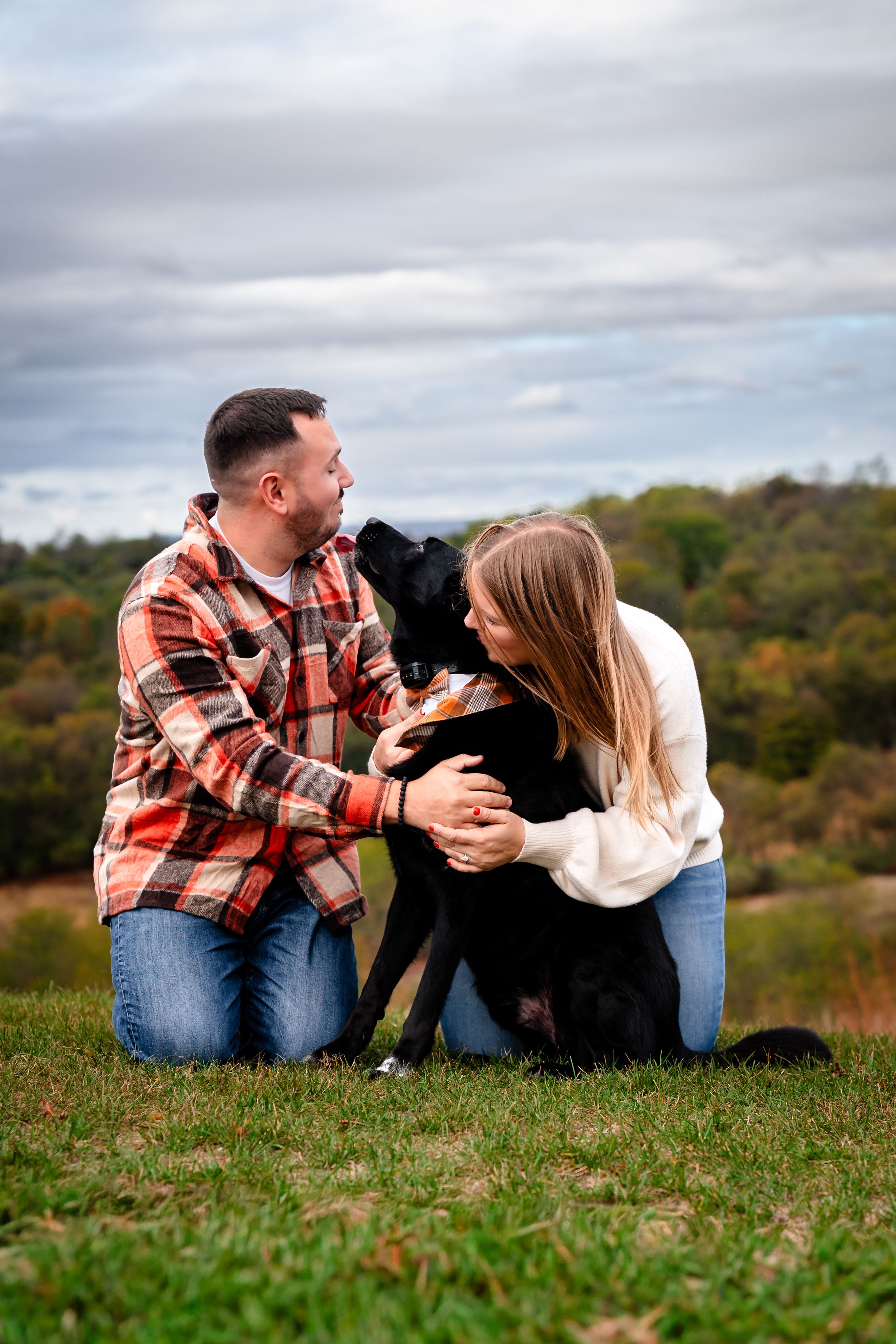 Happy couple playing with their black dog during outdoor fall photoshoot.