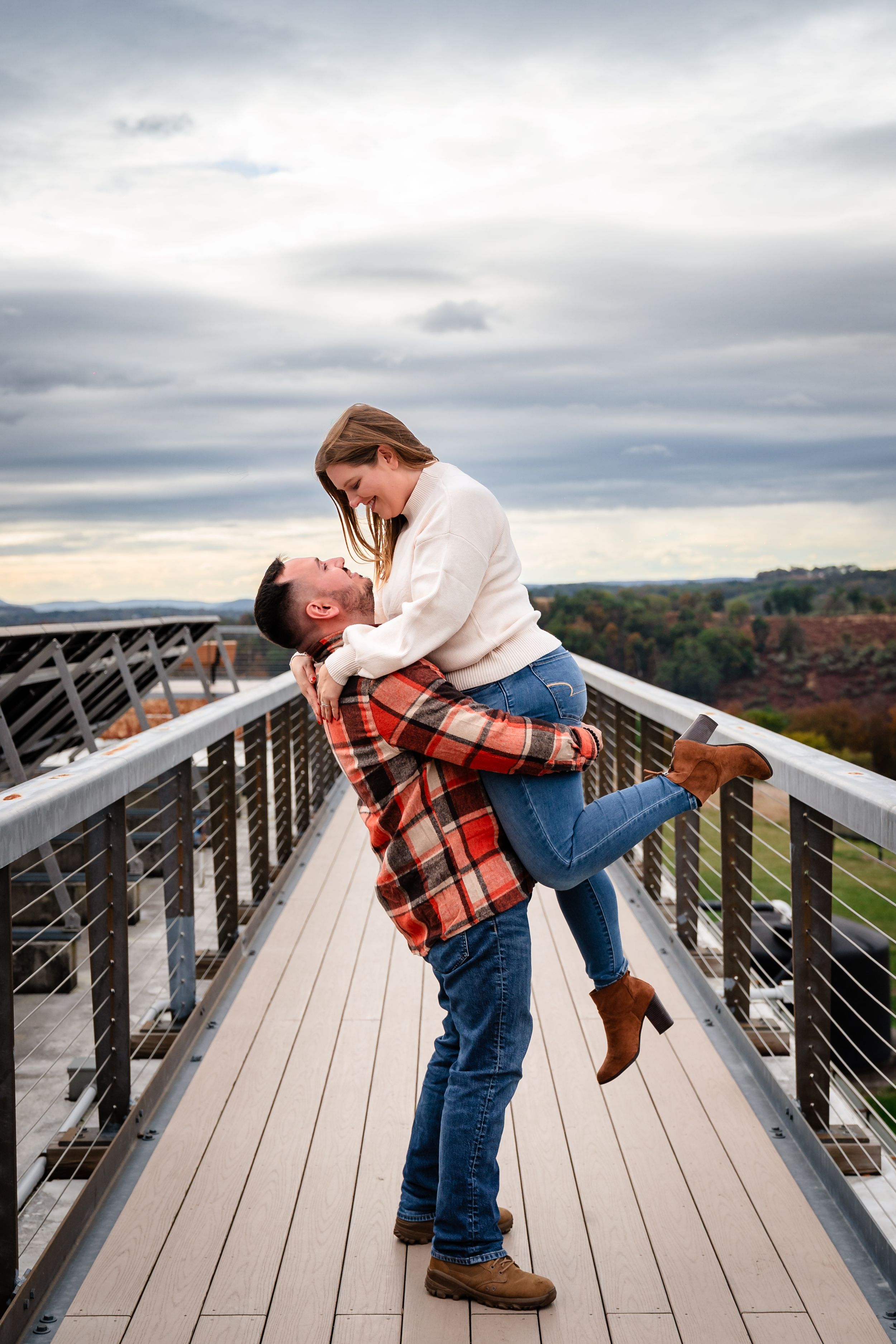Romantic couple sharing playful moment on wooden observation deck with cloudy sky.