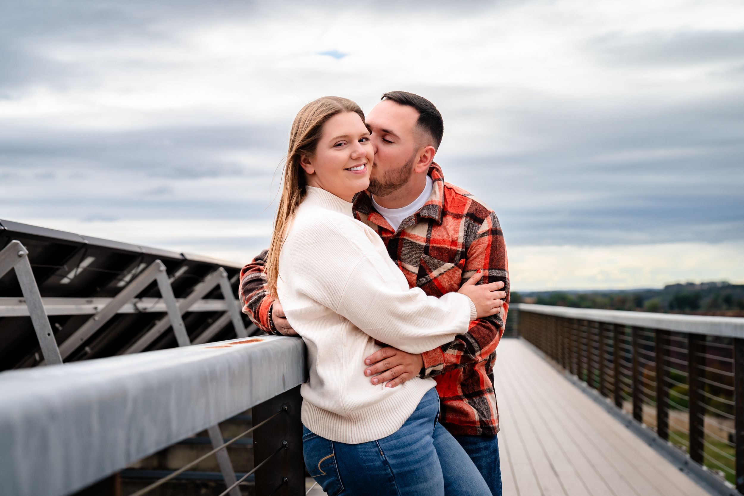 Intimate moment between couple on wooden bridge during cloudy autumn day.