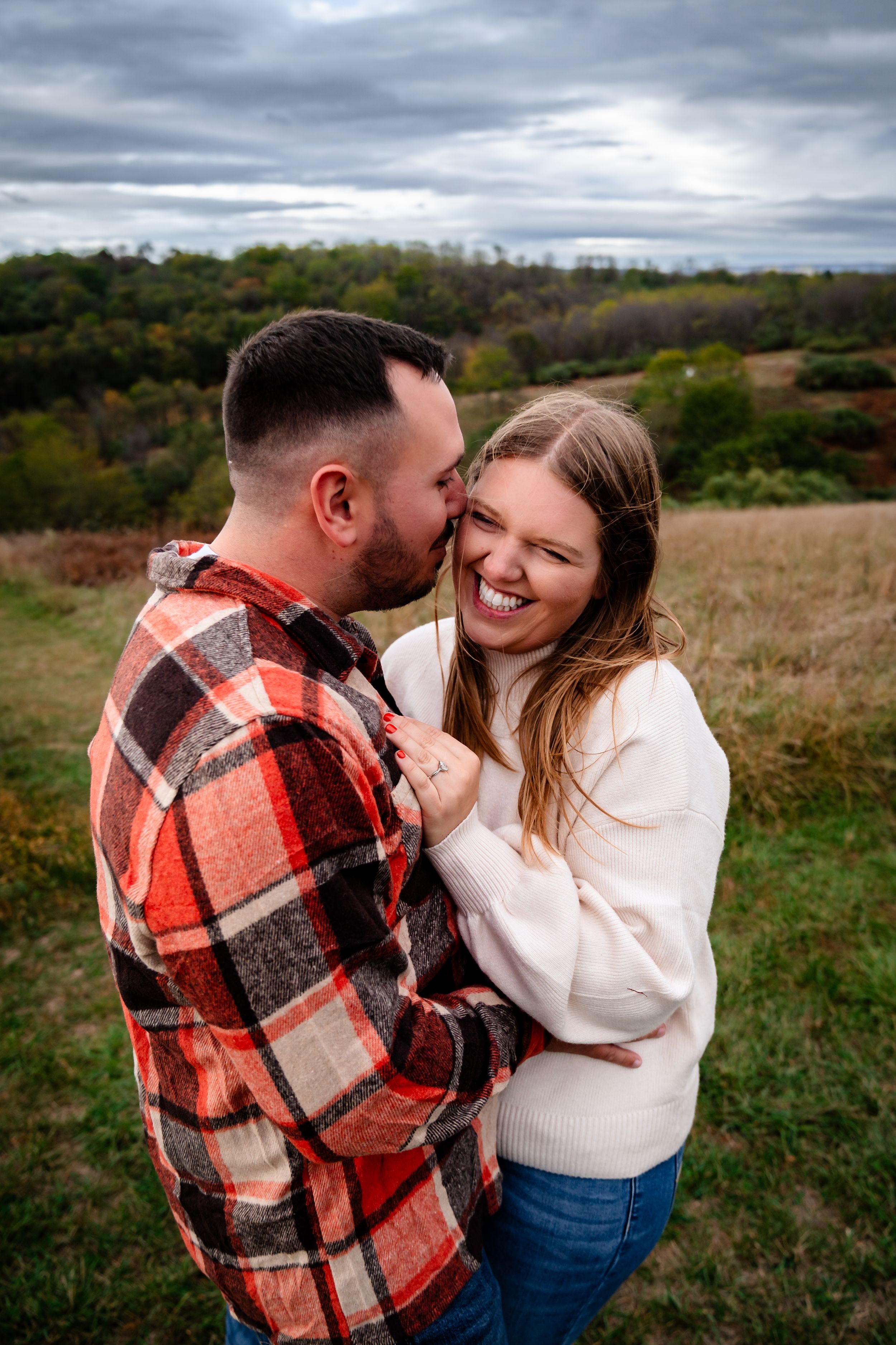 A romantic moment shared between a couple in a rustic field on an overcast day.