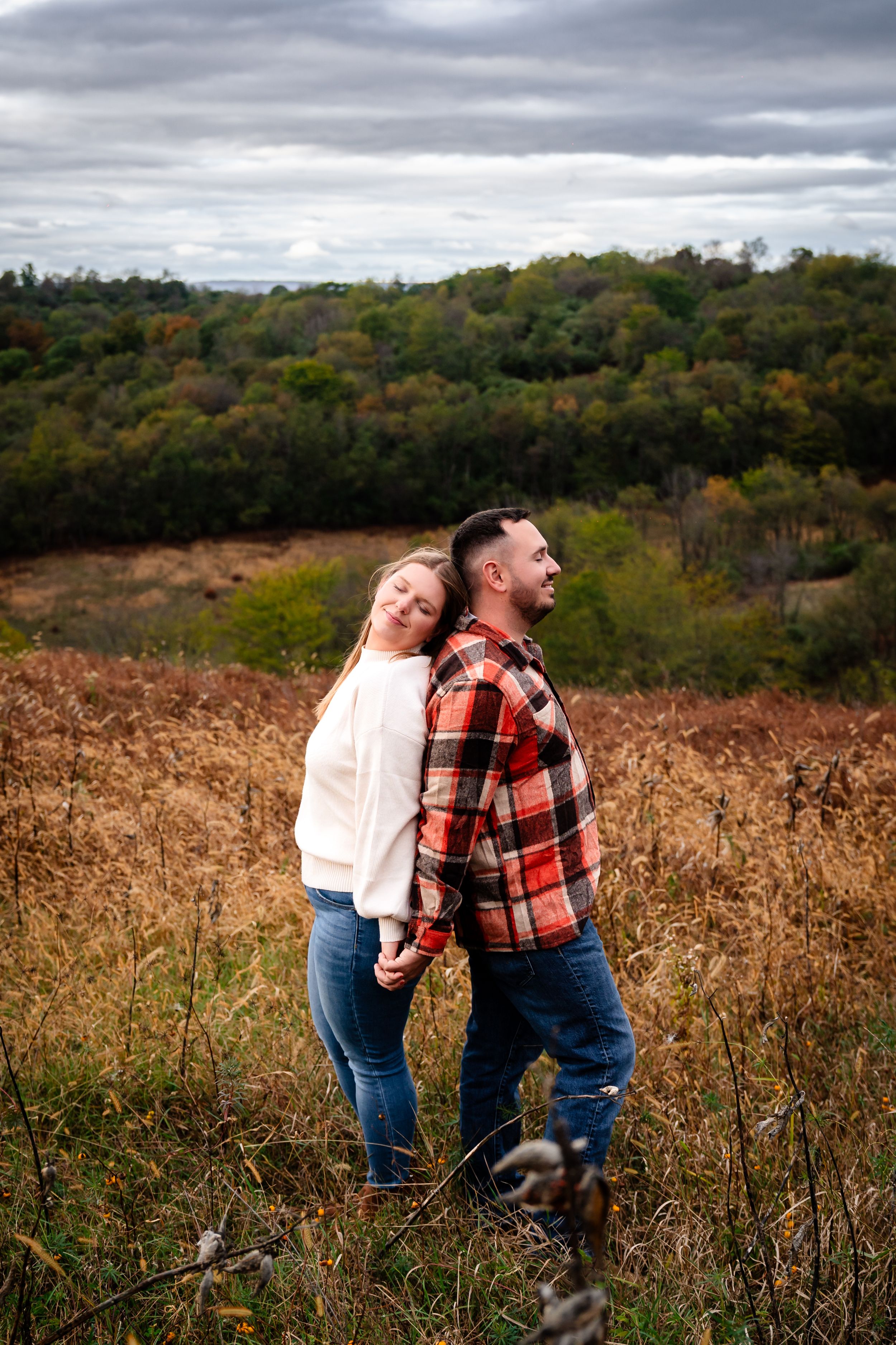 A couple shares a playful moment in a field of tall grass under moody autumn skies.