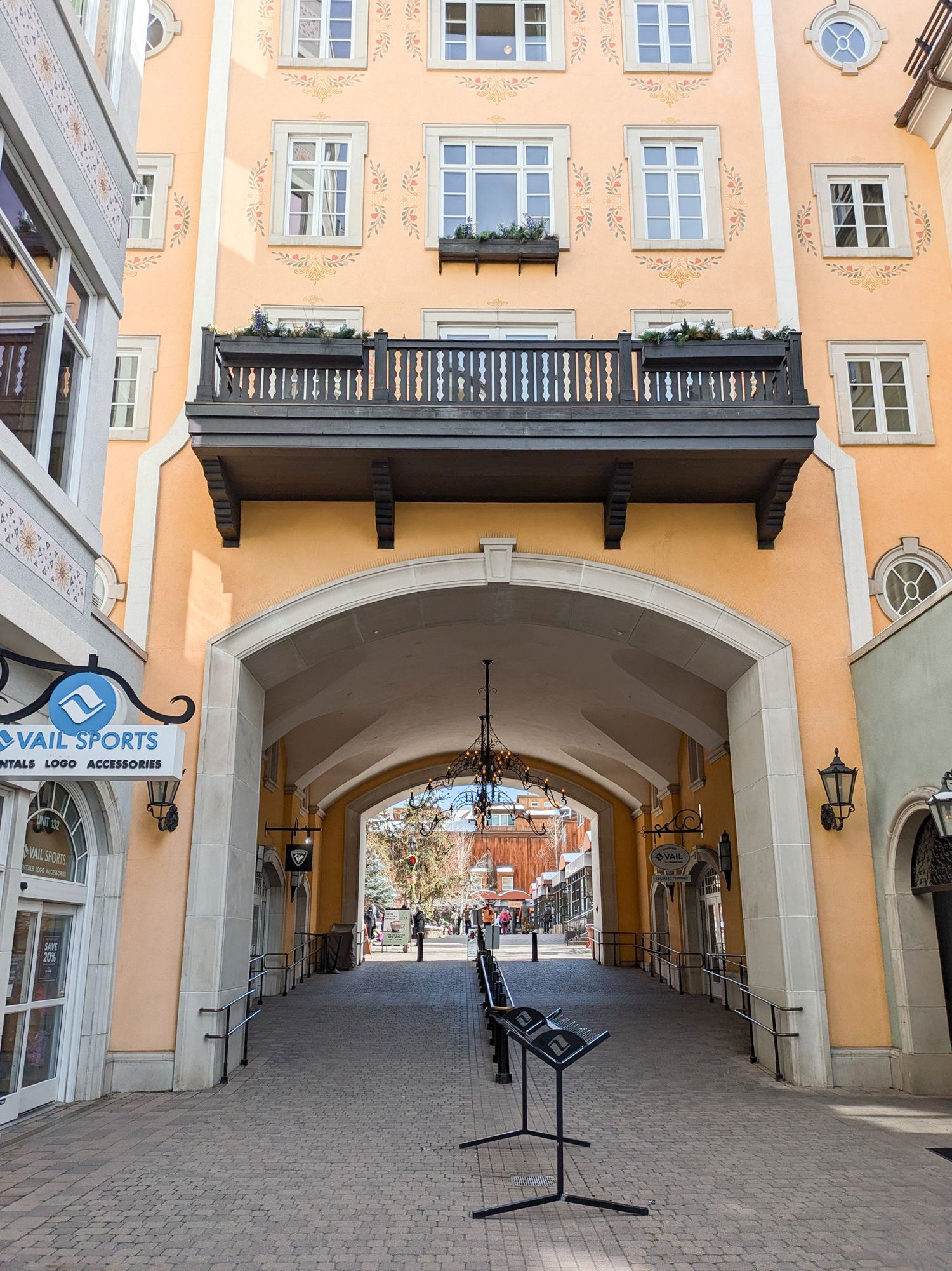 A charming archway passage in a peach-colored building with a black balcony and lanterns in a European city street.