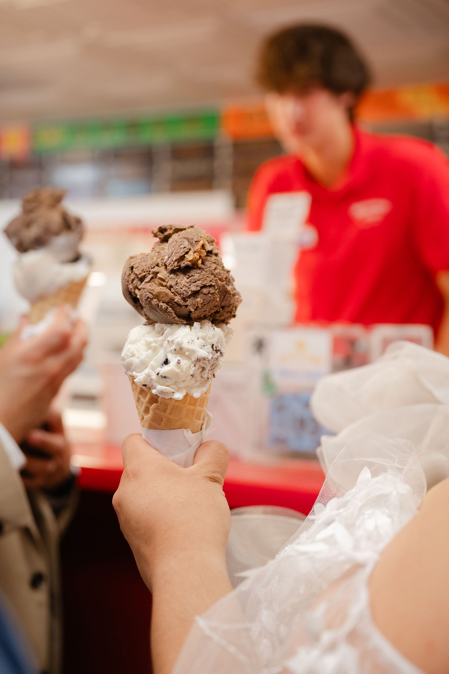 Ice cream cones with chocolate and vanilla scoops being held up in a row against a blurred background.