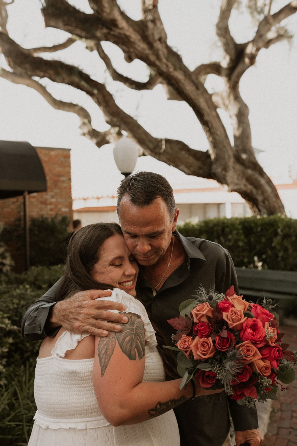A romantic outdoor photo session featuring a white dress, coral roses, and tender embraces under twisted tree branches.