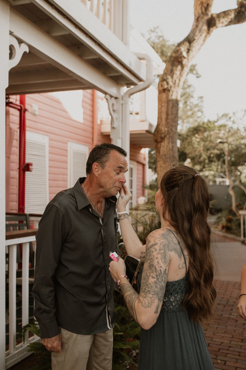 A couple shares an intimate moment together on a brick walkway outside a house with white trim.