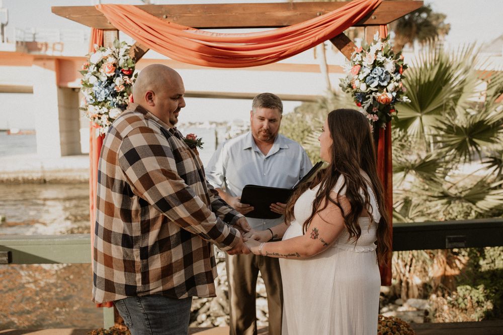 A couple embraces during their sunset desert wedding ceremony under a copper-colored fabric canopy.