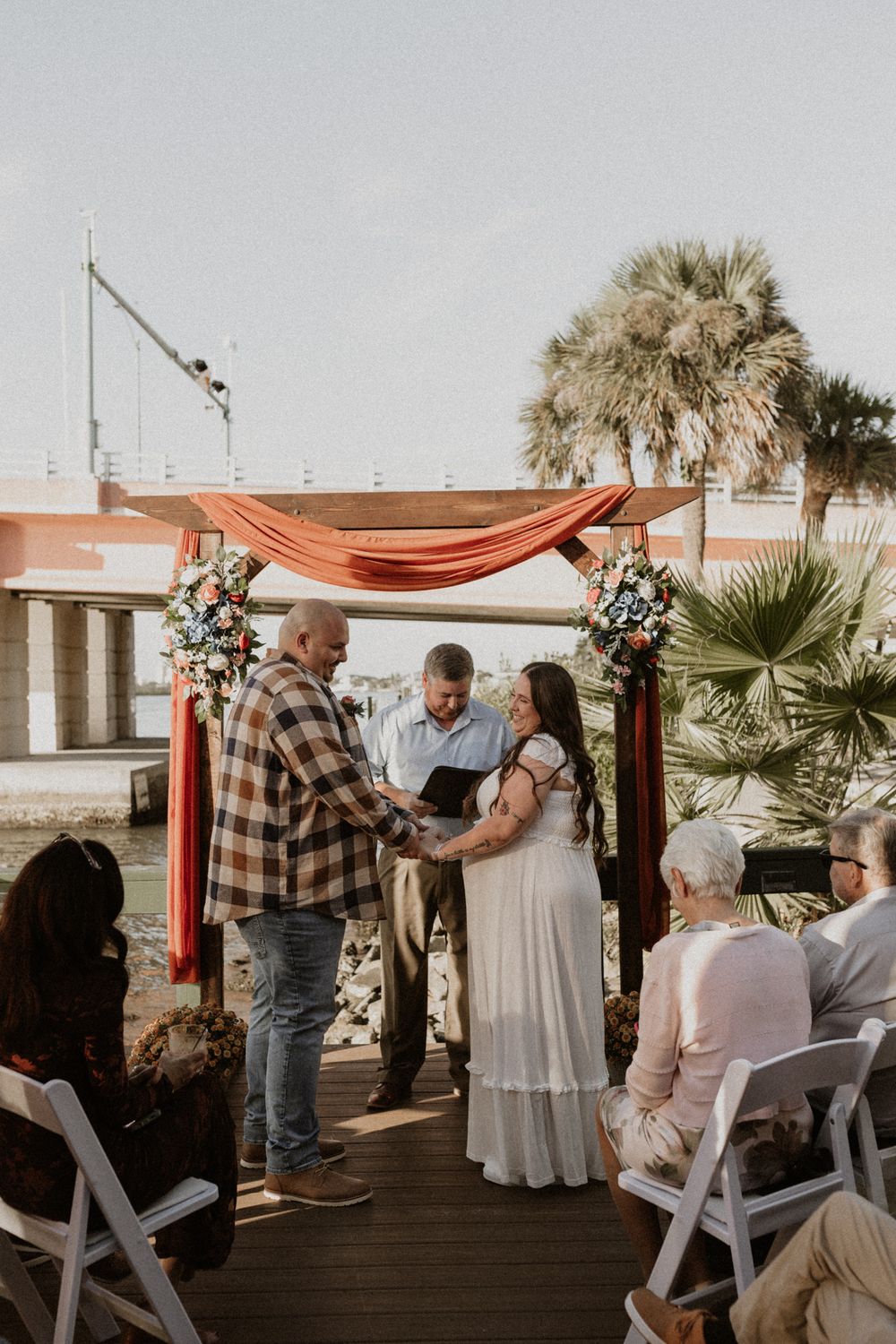 An outdoor wedding ceremony setup with coral draping and white chairs by the waterfront.