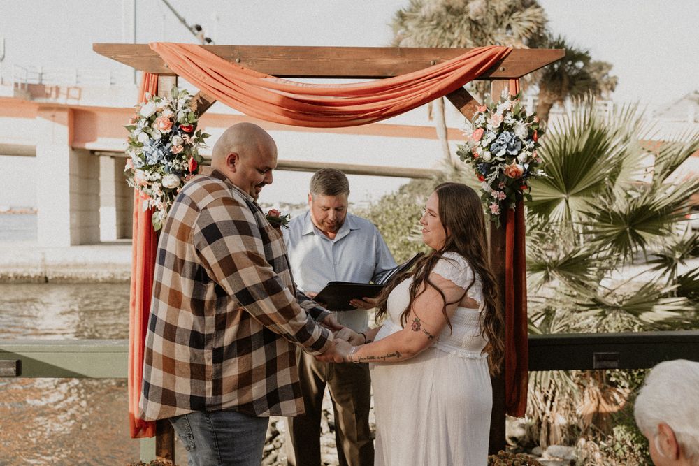 A couple shares a romantic moment during a sunset photoshoot in a rustic outdoor setting with palm trees.