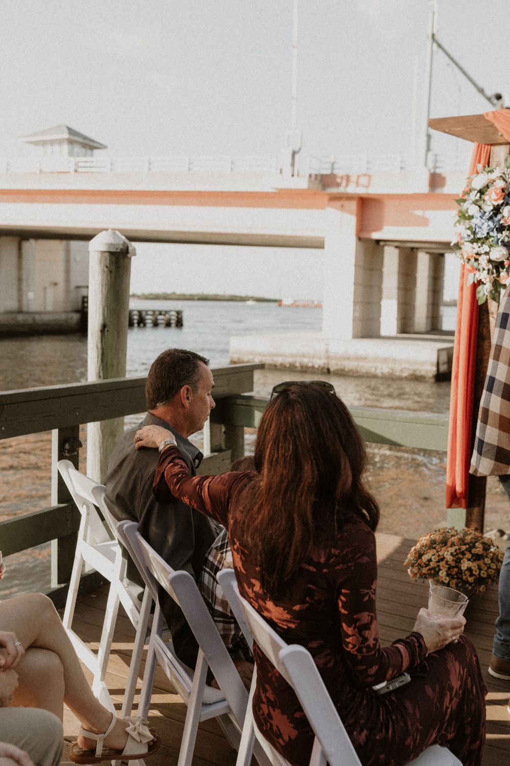 Couple shares intimate moment on wooden deck overlooking waterfront at sunset.
