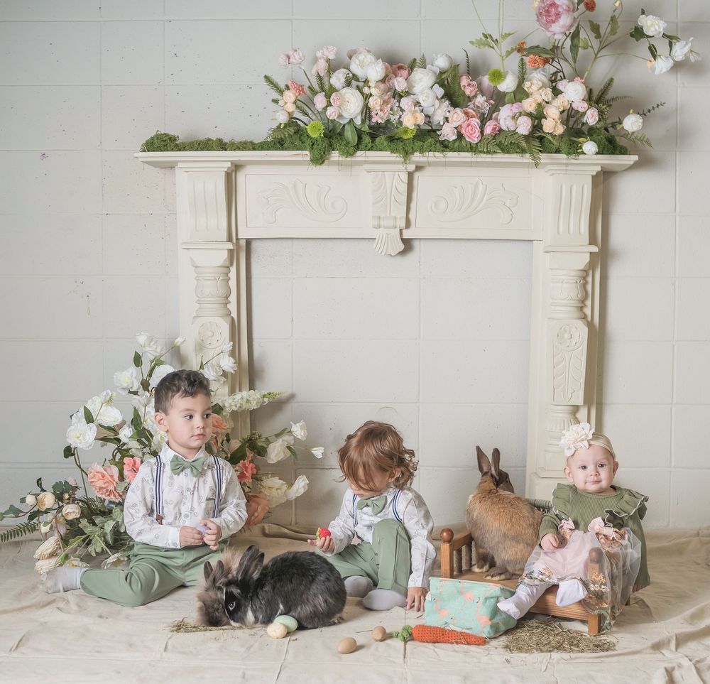 Vintage white fireplace mantel decorated with pink floral arrangements and baby props for professional photography setup.