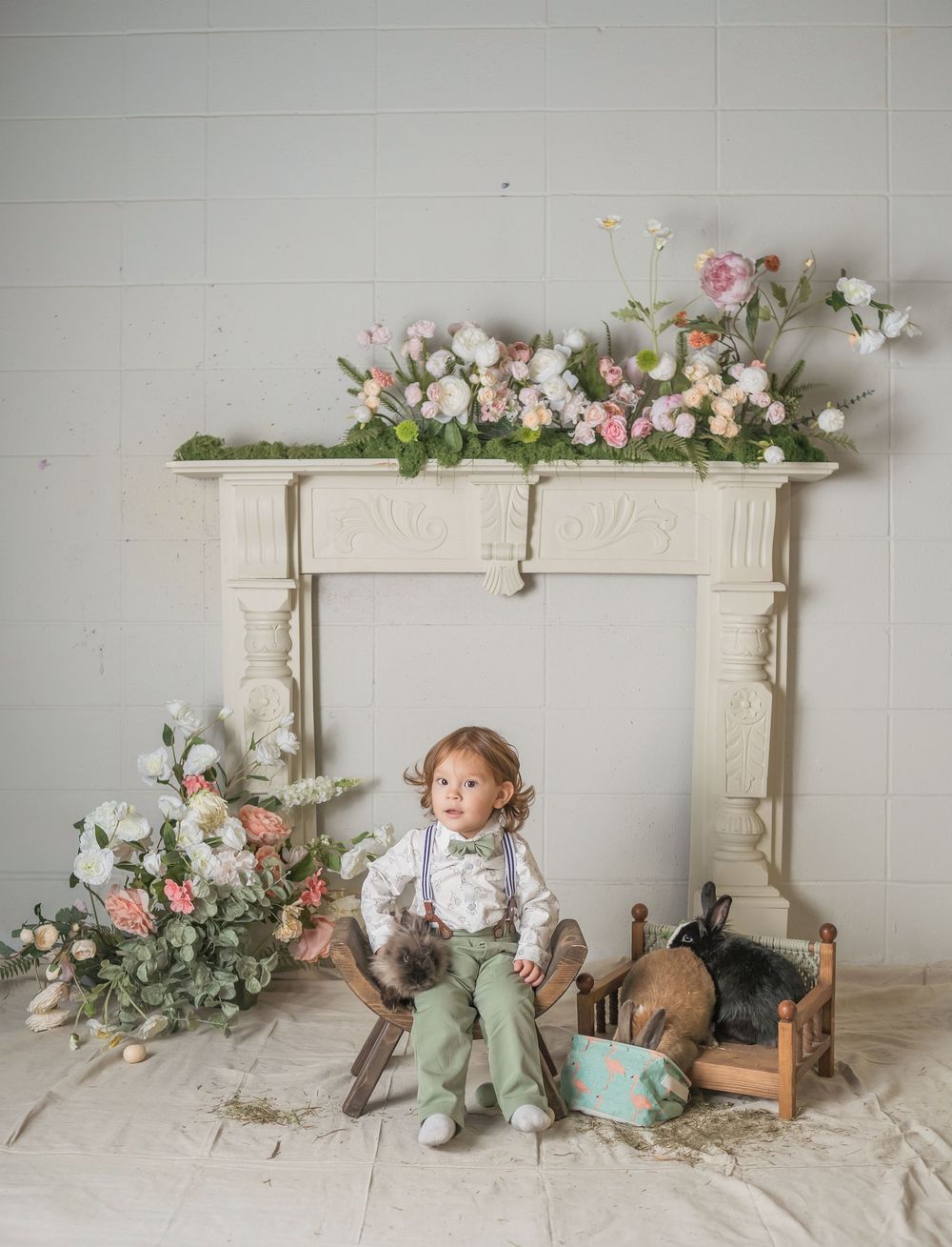 Vintage white fireplace mantel decorated with pink and white flowers, with rustic toys and decor arranged below.
