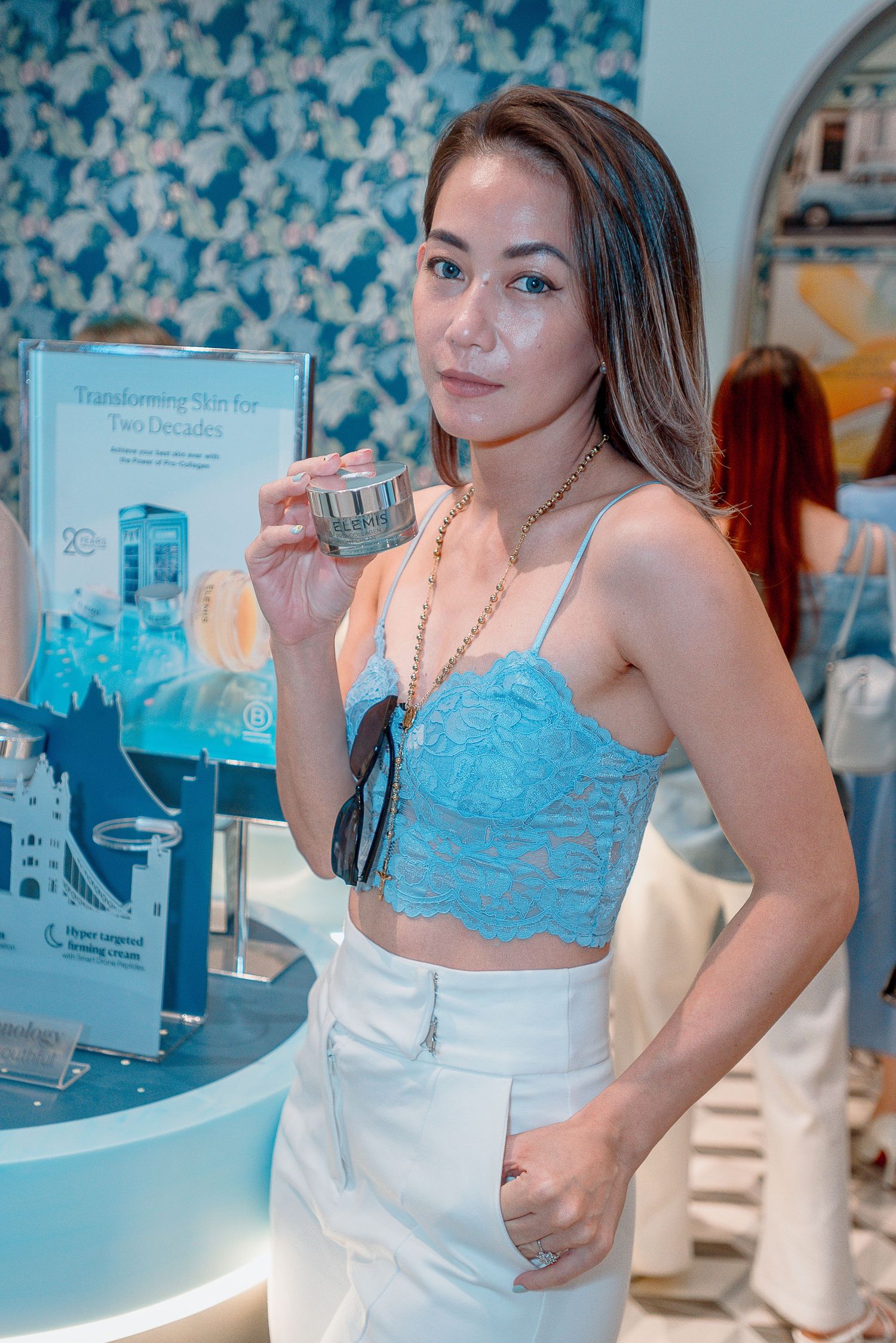 Person wearing a light blue top and white apron poses in front of a counter in a retail or restaurant setting.