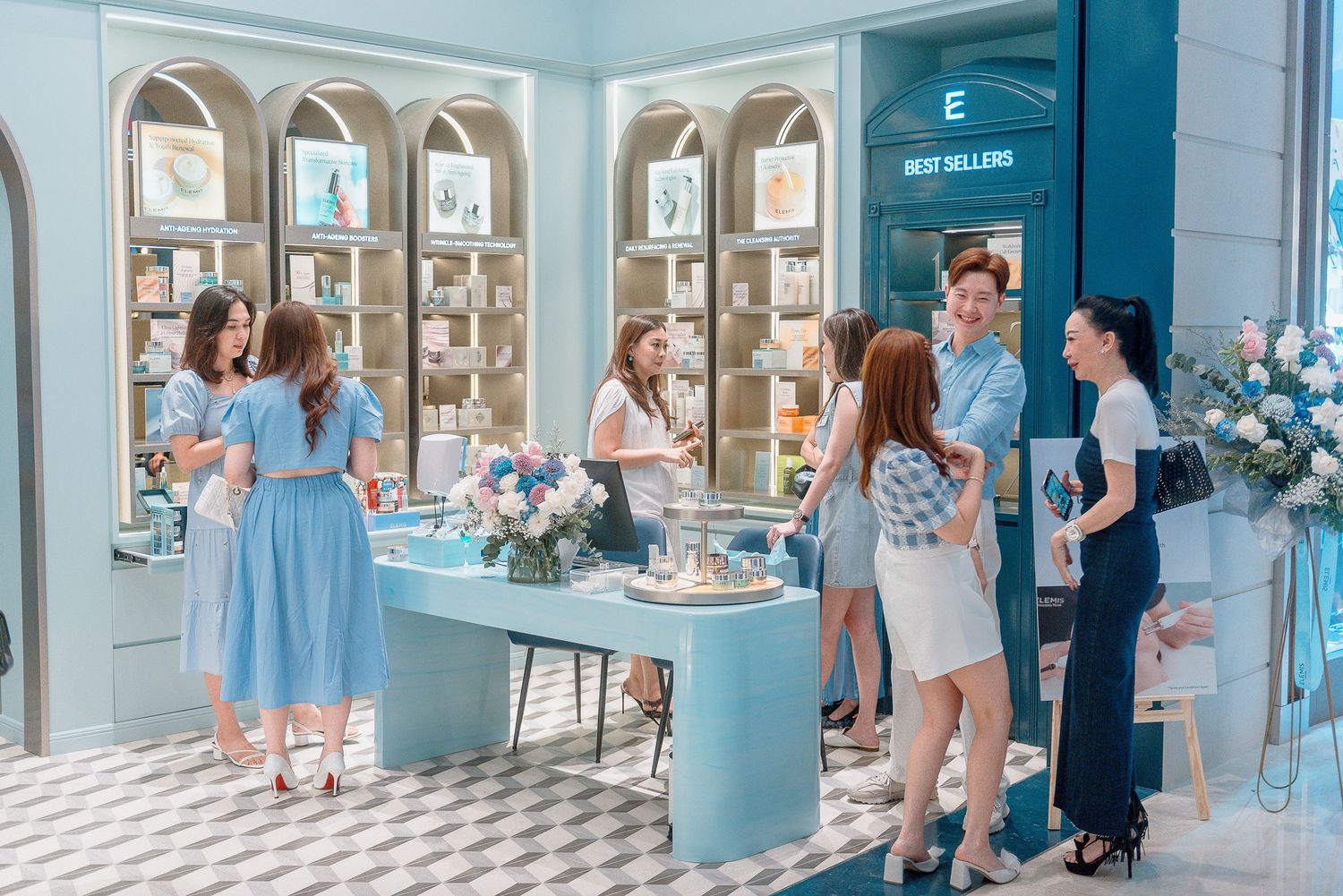 A panoramic view of a light blue interior space with checkered floors and people browsing display cases along the walls.