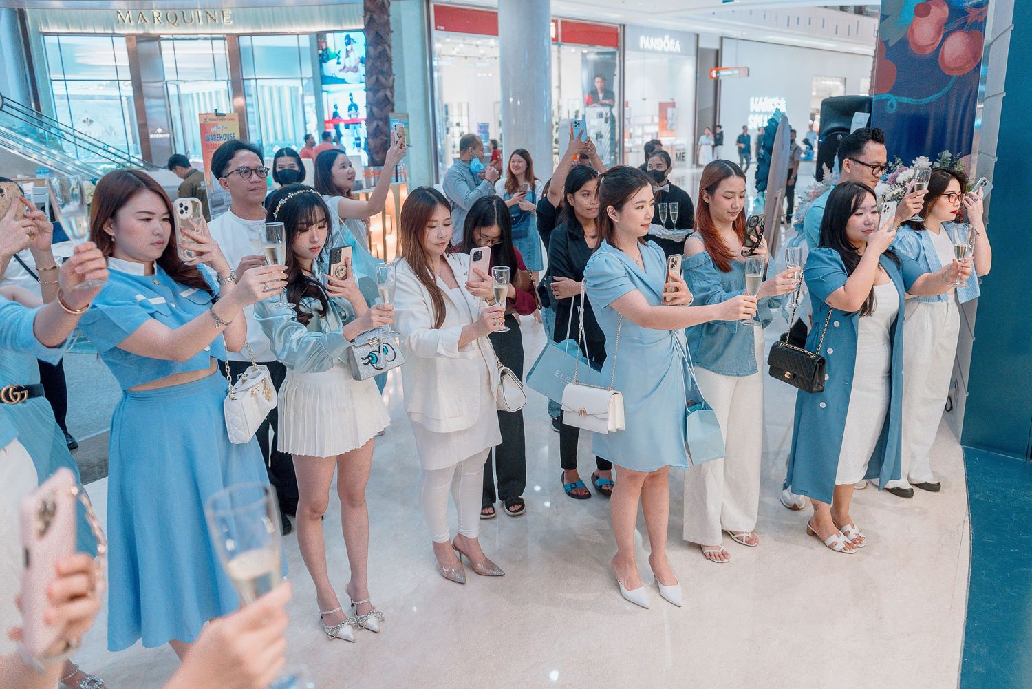 A group of people in blue and white outfits stand together at an event, raising their hands in unison.
