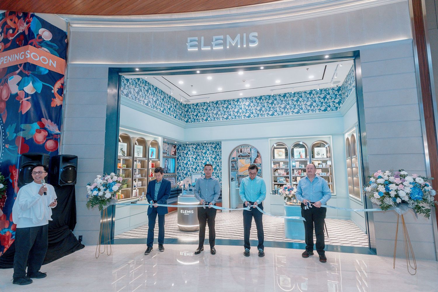 A bright blue and white Elemis beauty store storefront with staff standing outside in a shopping mall.