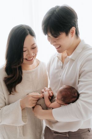 A loving couple in white clothing share a tender moment with their newborn baby against a bright background.一對身穿白色服裝的恩愛夫婦在明亮的背景下，與他們的新生兒共享溫馨