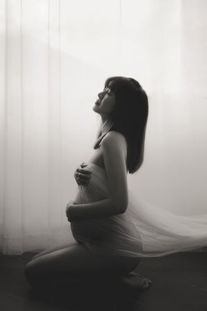 Artistic black and white maternity photo with soft draping fabric and dramatic lighting creating an ethereal silhouette黑白藝術孕婦照，柔和的垂墜面料和戲劇