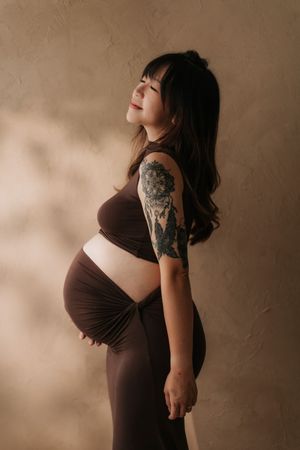 A series of sepia-toned photographs showing a pregnant woman in a brown dress against a textured backdrop.一組棕褐色調的照片，照片中一位孕婦穿著棕色連身裙，背景是紋理豐富的