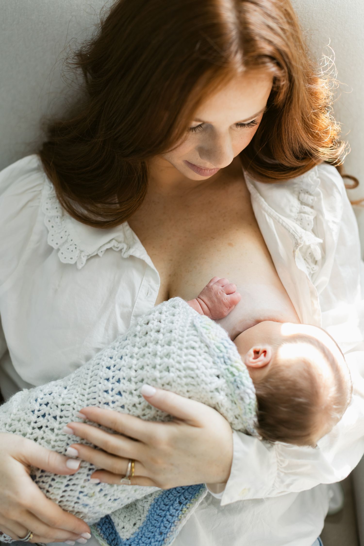 Red haired mother breast feeds newborn swaddles in crochet blanket during newborn photos. Portsmouth, Rye, Woodstock newborn photographer