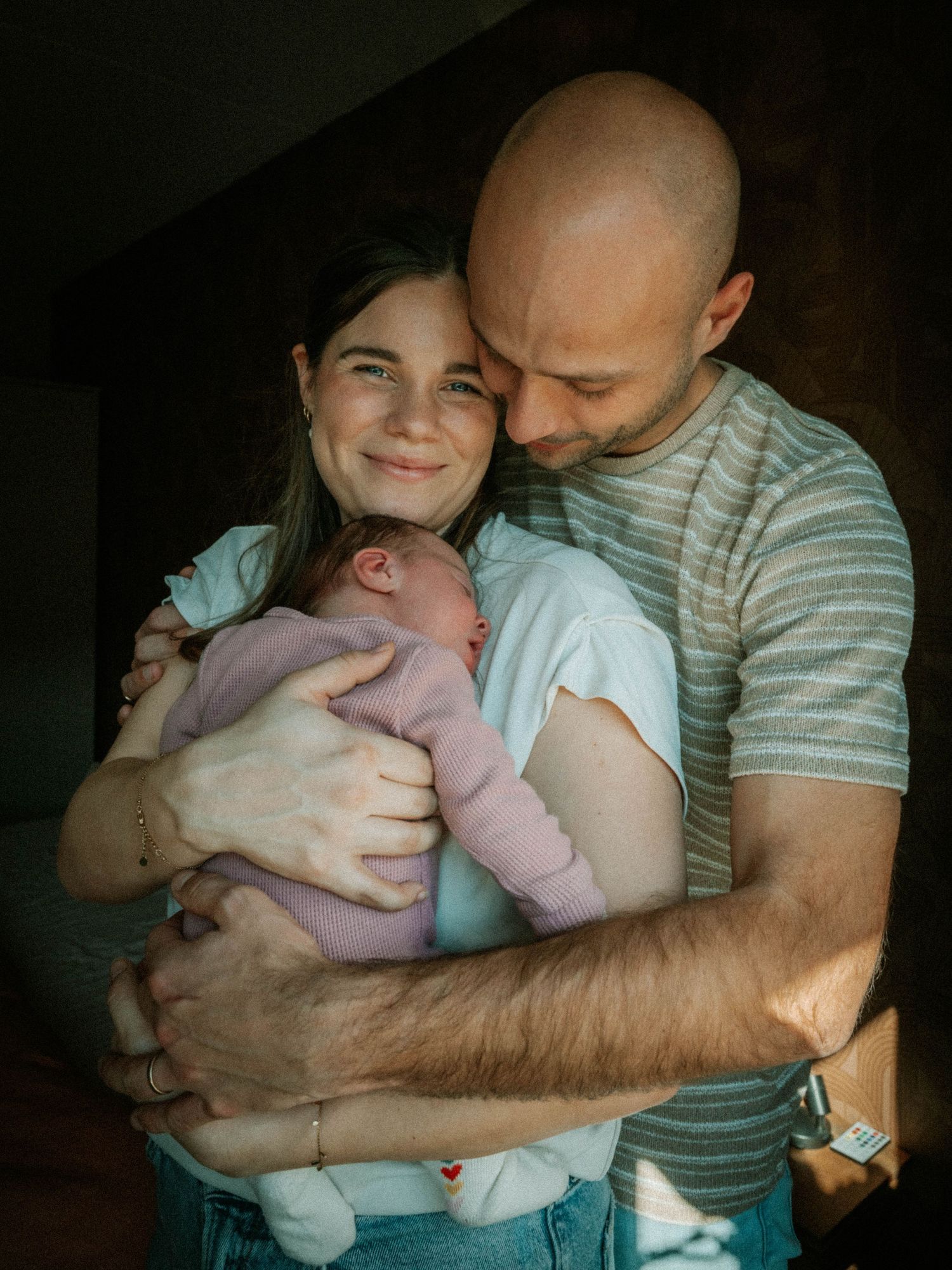 Happy couple tenderly embracing their newborn baby at home, sharing a joyful family moment.