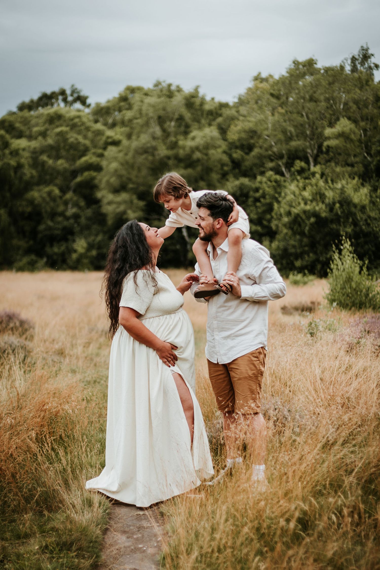 A couple shares romantic moments in a golden field during sunset as they dance and embrace in white and brown attire.