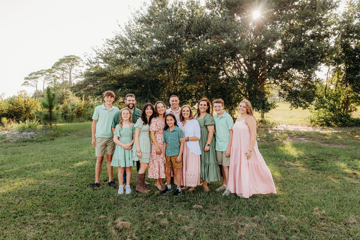 Family group wearing coordinated pink and green outfits poses together on sunny beach at sunset.