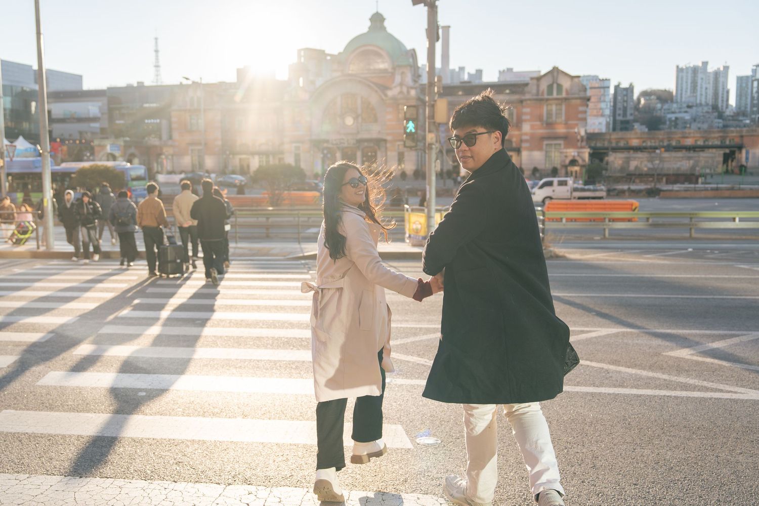 A couple walks together holding hands on a sunny urban street at golden hour with long shadows on the pavement.