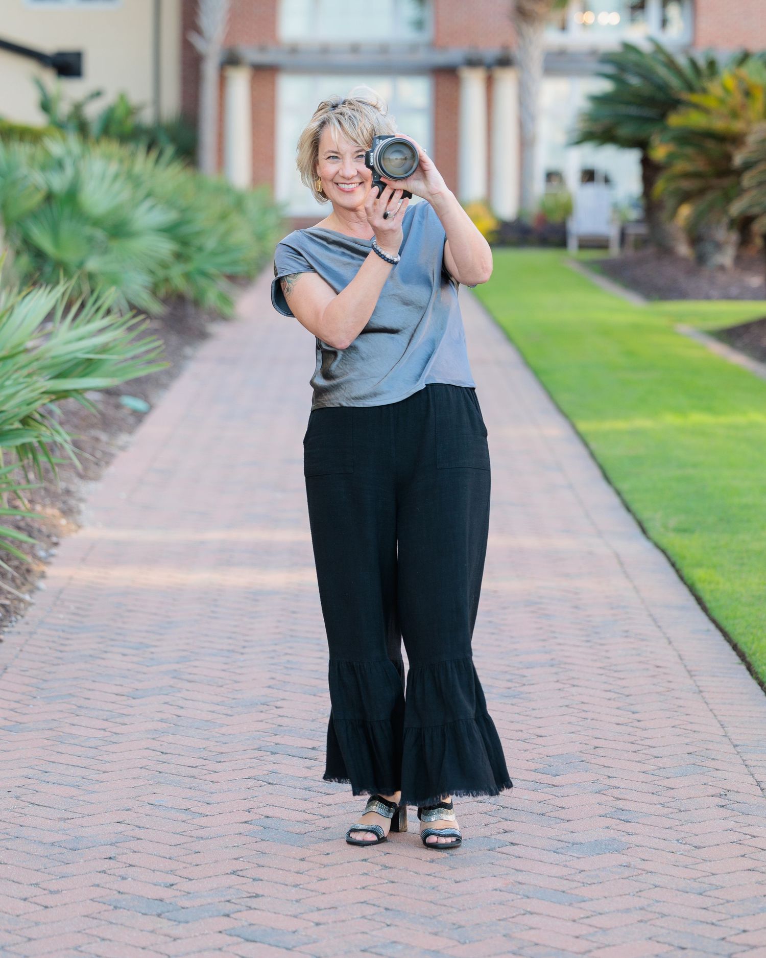 Professional photographer with camera capturing moments on a brick pathway surrounded by palm trees and greenery.