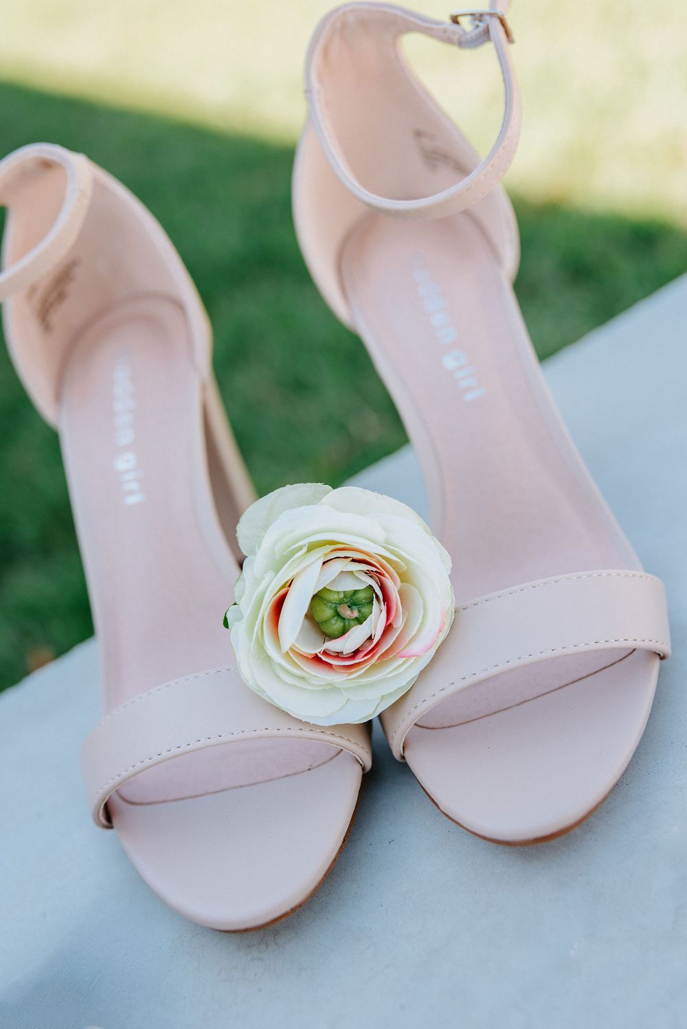 Elegant pink leather sandals adorned with delicate white ranunculus flowers displayed on a soft blue surface.