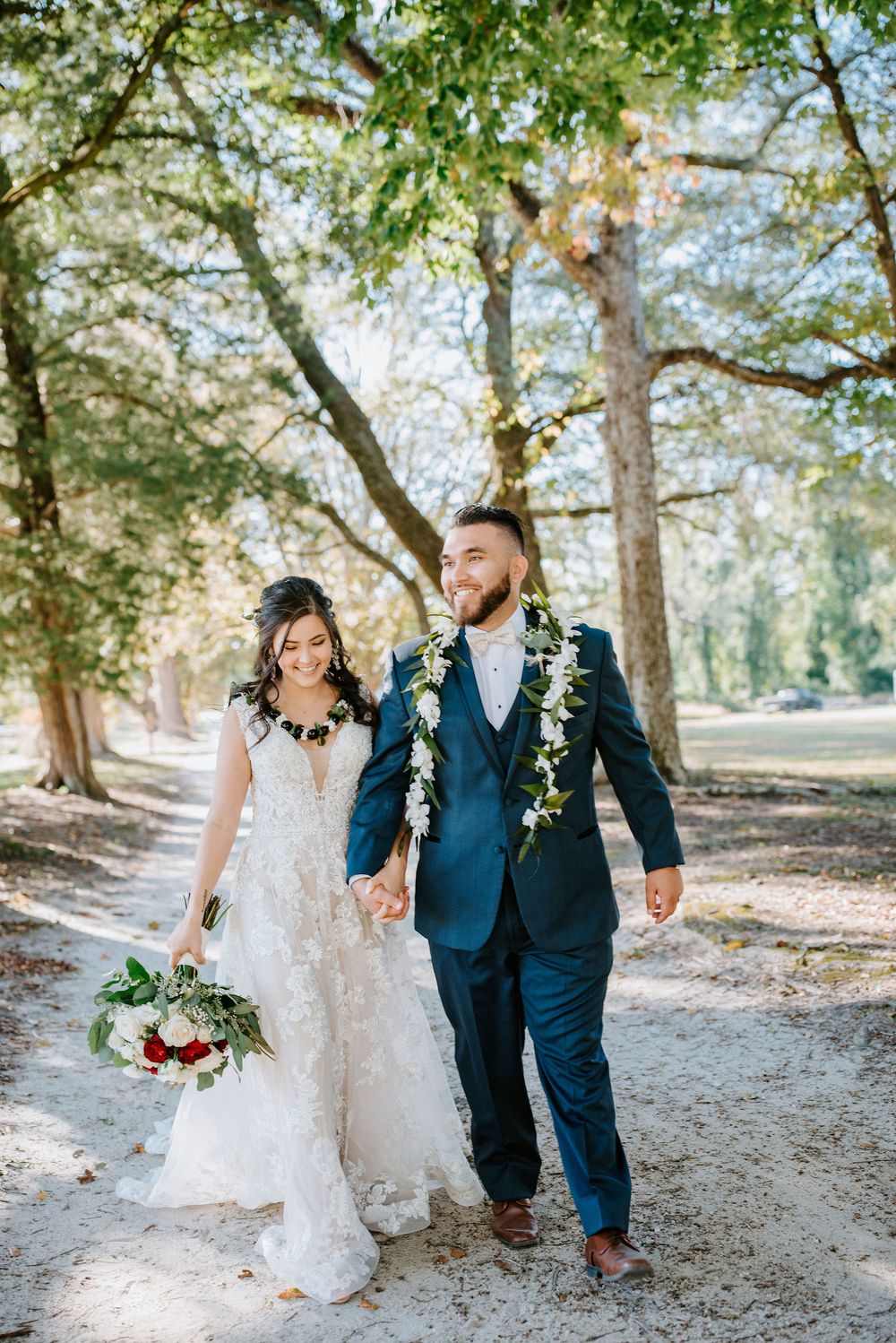 Newlyweds walk together along a tree-lined path on their wedding day in romantic outdoor setting.