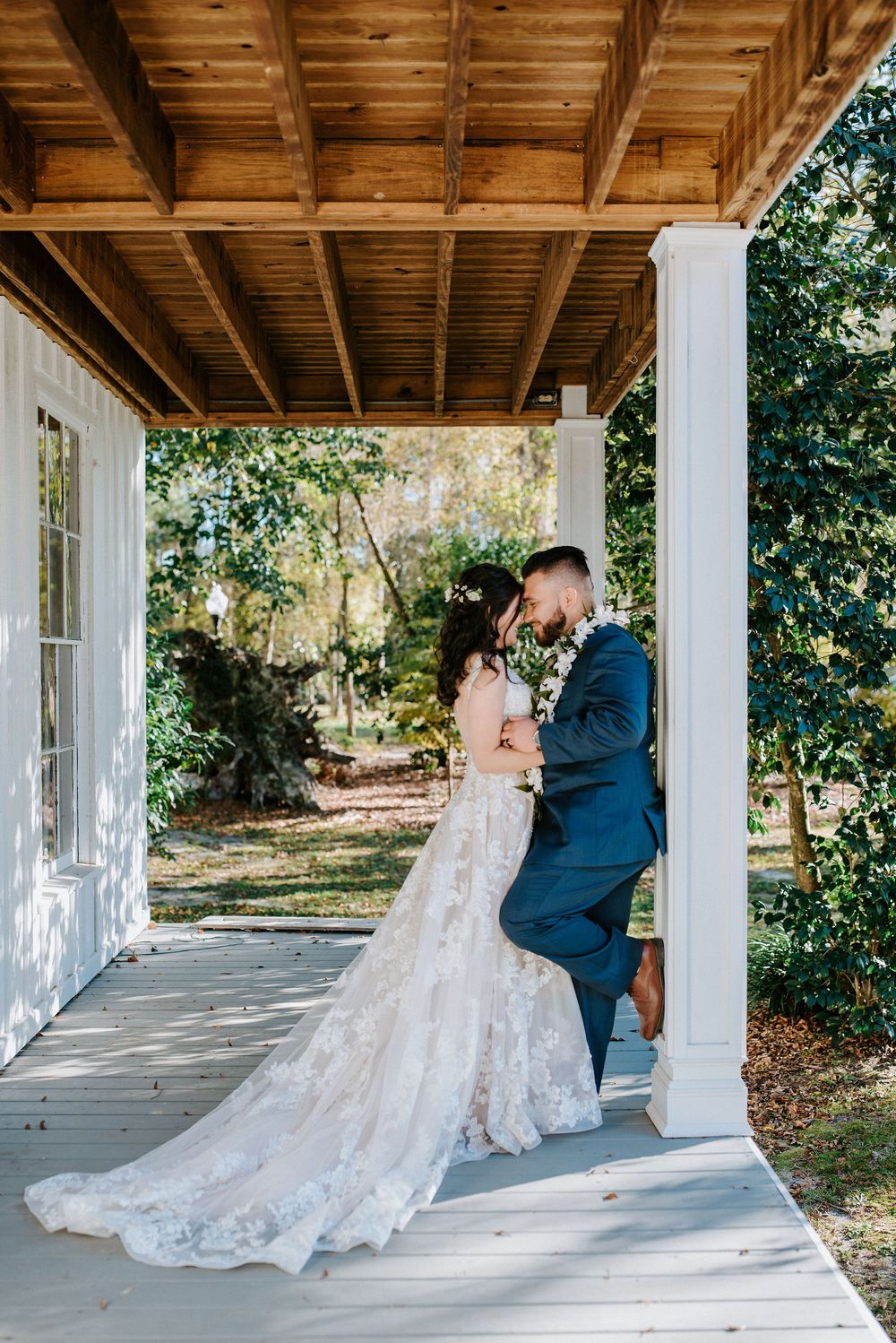 Romantic wedding couple shares intimate first look moment on a rustic covered porch with wooden beams and white columns.