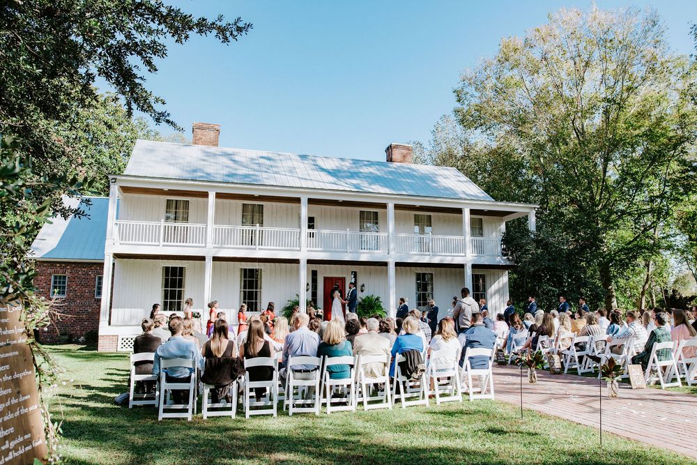 White chairs arranged in rows for an outdoor wedding ceremony at a historic farmhouse venue with wraparound porch.