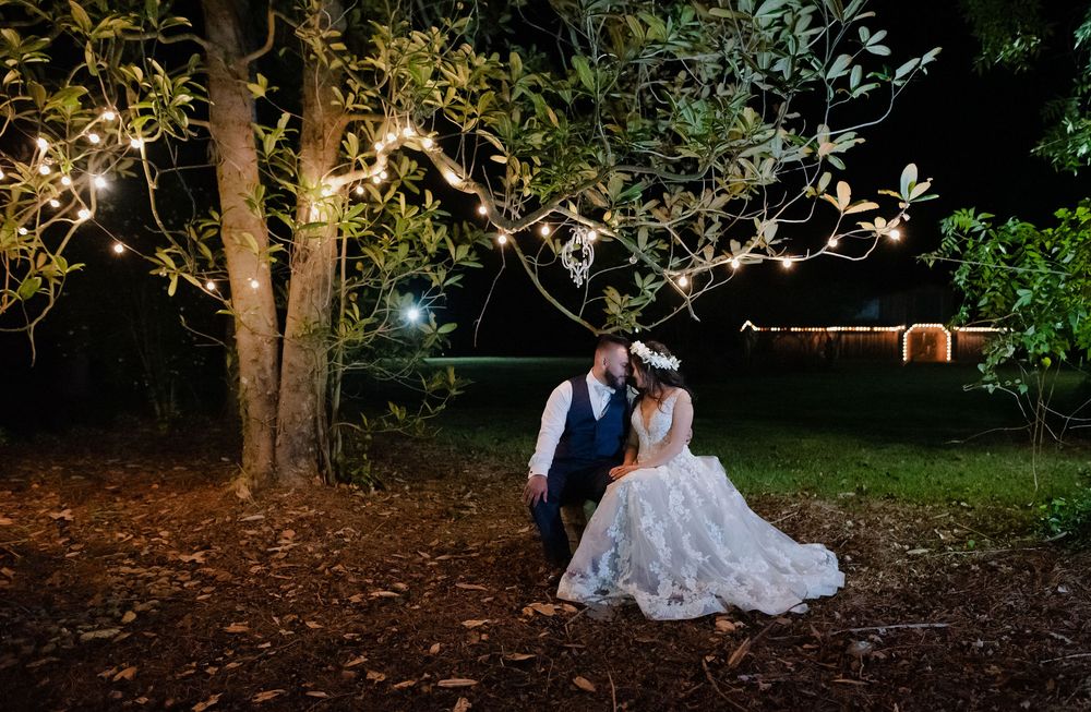 A romantic evening wedding photo under twinkling lights and trees in a garden setting.