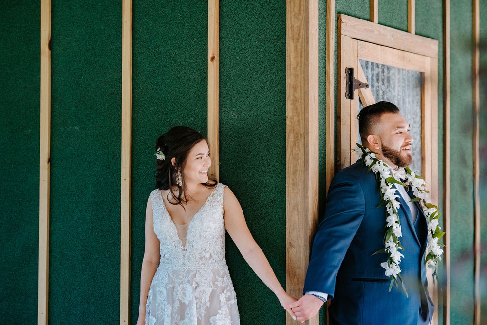 Wedding couple poses against emerald green wall in elegant attire during their special day.