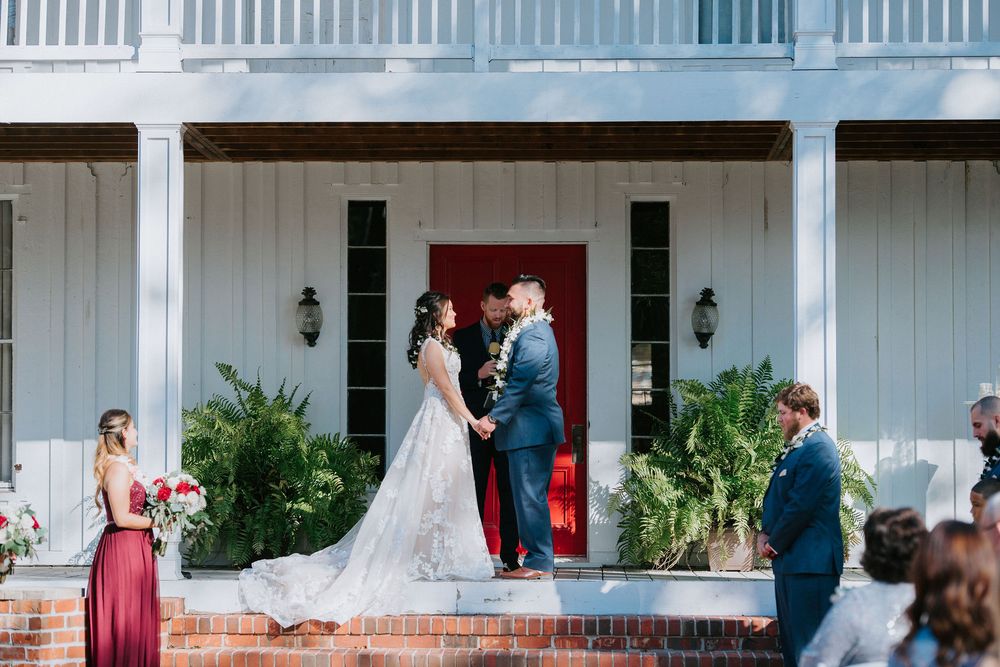 A wedding ceremony taking place on a classic white plantation-style porch with red door.