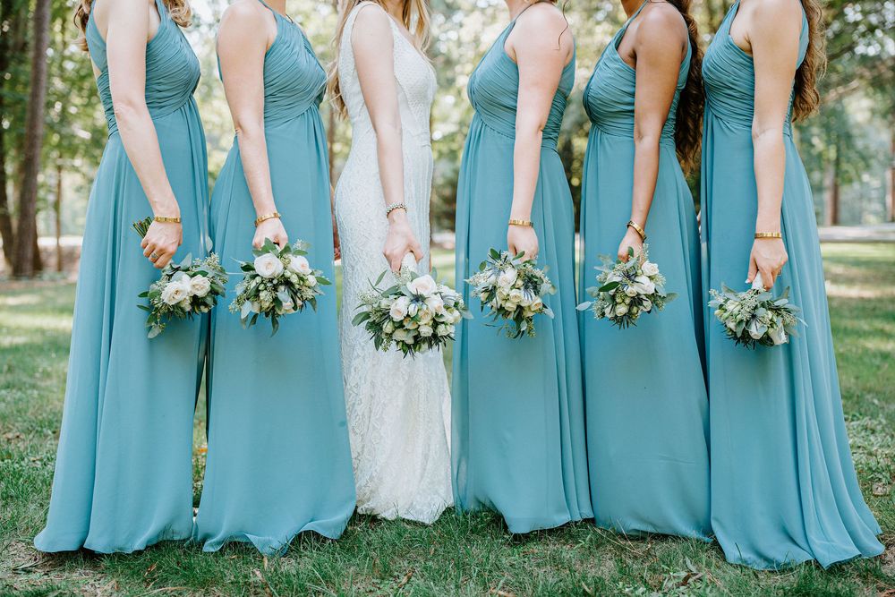 Wedding party in turquoise bridesmaid dresses and white bridal gown pose together outdoors with floral bouquets.