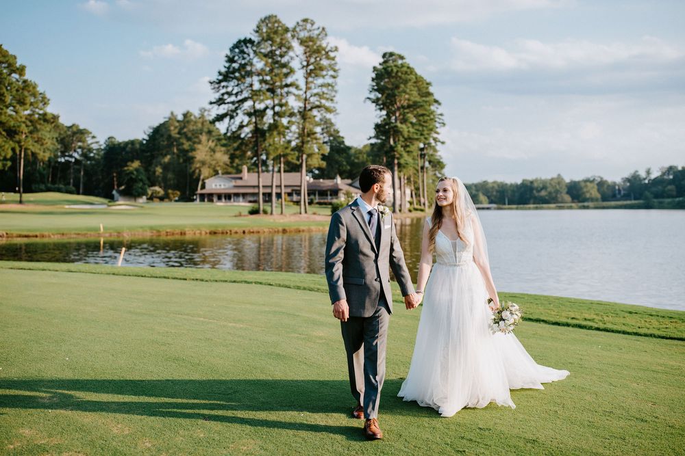 Couple walking together on a scenic golf course by a lake during a wedding photo session.