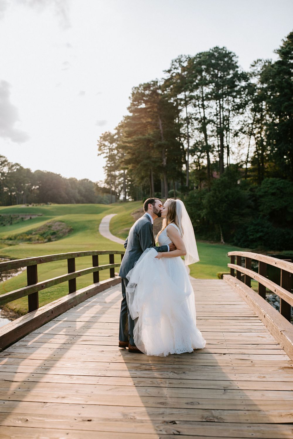 Newlyweds share romantic moments on a wooden bridge at a golf course during golden hour.