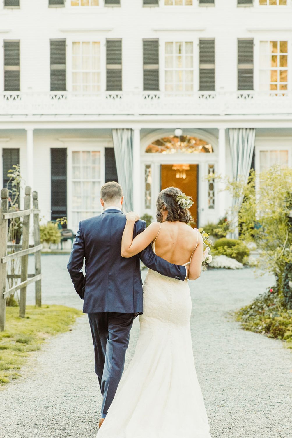 A couple walking towards a grand white mansion on a gravel path.